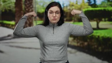 Parktaki kadın kollarını kavuşturarak gücünü gösteriyor. Çevresi yeşilliklerle çevrili. Açık havada güçlü ve eğlenceli bir an yakalıyor..