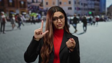 Kırmızı elbiseli bir kadın kalabalık bir caddede zavallı bir jest yapıyor. Bulanık bir şehir geçmişine karşı etkileyici vücut dili ve kendinden emin bir ifade sergiliyor..