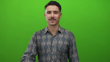 Kalıplı tişörtlü genç İspanyol adam canlı yeşil arka planda izole edilmiş. Stüdyo ortamında olumlu ve onaylı el hareketleriyle iyi bir hareket yapıyor.