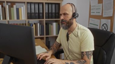 Ofiste çalışan İspanyol bir adam kameraya gülümseyen bir kulaklık takıyor kolları çaprazlanmış kitaplarla çevrili bir şekilde kapalı bir iş yerinde.