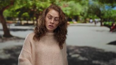 Güneşli bir günde arka planda bulanık bir kadın gözlük ve süveter takıyor..