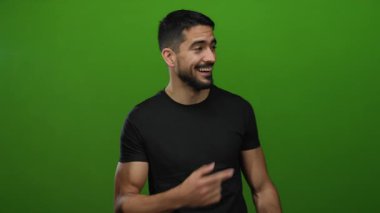 Genç adam, izole edilmiş yeşil bir arkaplanda gülümseyip işaret ederek, mesleki ya da gelişigüzel ifadeler ve tarz sergileyen, olumlu ve çekici bir tavır sergiliyor.