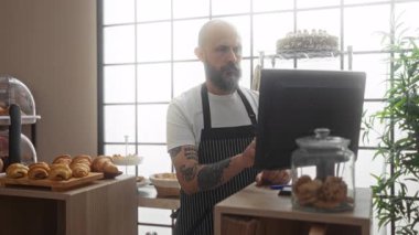 Pastanede çalışan bir adam bilgisayarı kontrol ediyor. İki eli yüzü üzerinde. Tezgahta duran kurabiye ve kurabiyelerle çevrili stresi ifade ediyor.