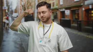 Sakallı ve steteskoplu beyaz önlüklü, açık hava güvenini gösteren beyaz önlüklü, şehrin arka planında gururla kolunu esnetiyor..