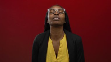 Kadın gülümsüyor ve canlı kırmızı bir arka plana öpücük yolluyor. Güzelliğini ve pozitifliğini güven ve neşeyle gösteriyor..