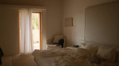 Lüks yatak odası beyaz çarşaflı yapılmamış yatak odası ve güneşli bir veranda kapısının yanındaki davetkar koltuk, konfor ve zarafeti huzurlu Akdeniz atmosferiyle harmanlıyor..