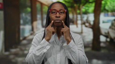 Gözlüklü bir kadın şehir caddesinde neşeli bir şekilde gülümserken yüzüne bakıp neşeli bir ifade takınıyor..