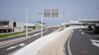 Lanzarote, İspanya 'da bulanık bir açık hava manzarası. Açık bir gökyüzünün altında, dağılmış yolları, sokak tabelalarını, binaları ve park edilmiş arabaları gösteriyor..