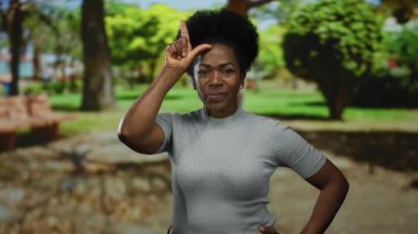 Parkta kendine güveni olan bir kadın, arka planda ağaçlar ve yeşilliklerle ezikçe bir jest yapıyor mizah ve basitliği resmediyor..