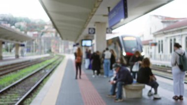 Yoğun bir tren istasyonunda tren ve şehir manzarasıyla bekleyen bulanık insanlar, modern bir çevrede seyahat ve beklenti hissi uyandırıyor..