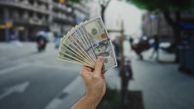 Bir şehir caddesinde dolarları elinde tutan bir adam, Amerikan banknotlarını sergiliyor, açık havada şehir ortamında.