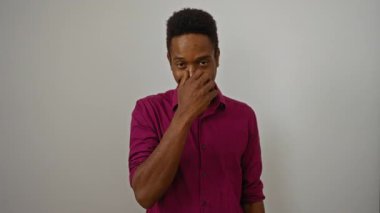 Parlak tebessümlü, eflatun gömlekli genç bir adam beyaz bir arka plana karşı duruyor, kendine güveni ve cazibesi var.