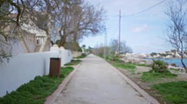 Açık bir günde, Akdeniz kıyısı boyunca ağaçlar ve uzak binalarla çevrili, dağılmış bir patikayla Mallorca 'da bulanık gezinti..