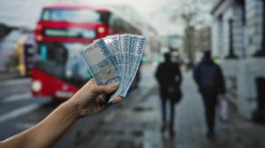 Açık hava otobüs durağında arka planda bulanık otobüsler ve yayalar olan Macar banknotları tutan bir adam günlük şehir yaşamını yakalıyor..