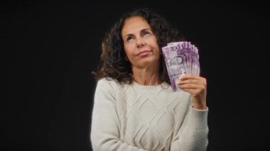 Filipinli pesoları elinde tutan kadın, izole edilmiş kara arka plana karşı yorgun görünüyor. Finans, yorgunluk ve orta yaşın özünü yakalıyor..