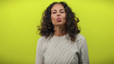 Kıvırcık saçlı olgun bir İspanyol kadın izole edilmiş sarı bir arka plana karşı süveter giyiyor ve elleriyle ifade ve duyguyu vurgulayan jestler yapıyor..