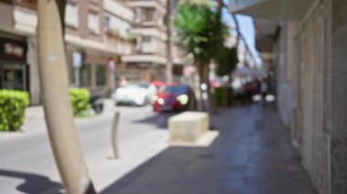 Bulanık binaların, arabaların, palmiye ağaçlarının ve yayaların bulunduğu bulanık sokak manzarası güneşli bir kentsel alanda.