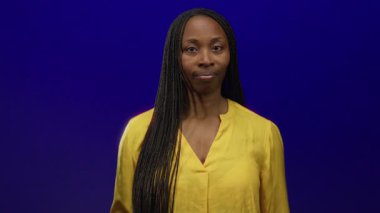 Sarı bluzlu, örgülü, mavi arka planda dikkatle seyreden, tetikte ve tetikte olan, tetikte olan, tetikte ve odaklanmış bir kadın..