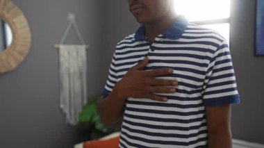 Gri duvarları, modern dekoru, çizgili gömleği ve doğal ışığı olan şık bir oturma odasında el ele tutuşan genç adam sakin ve içe dönük bir atmosfer yaratıyor..