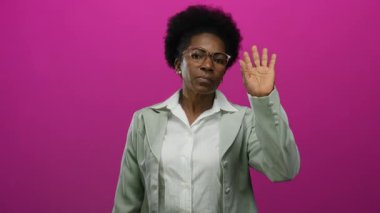 Gözlüklü, beyaz bluzlu ve yeşil ceketli bir kadın canlı pembe arka planda dalgalar oluşturarak iletişimi sembolize ediyor ve kendine güvenen mesleki davranışını vurguluyor.