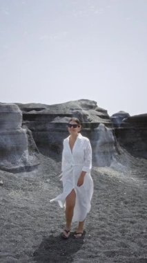 Lanzarote kanarya adalarında beyaz bir elbise ve güneş gözlüğü takmış volkanik bir arka planda yürüyen bir kadın.