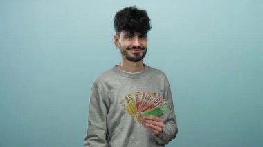 İzole edilmiş mavi arka plana karşı Norveçli kronu tutan adam, servetini güvenle gösteriyor.