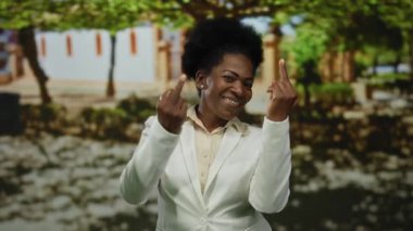 Parkta gülümseyen bir kadın arka planda ağaçlar ve gölgelerle el hareketleriyle dışarıdaki kaygısız sahneyi vurguluyor..