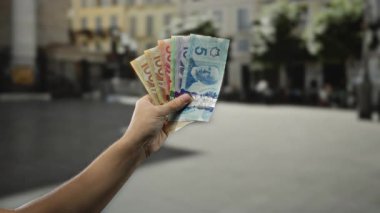 Bir şehir caddesinde elinde Kanada banknotları tutan adam, çeşitli finansal değerleri ve para birimlerini halka açık bir şehir ortamında sergiliyor..
