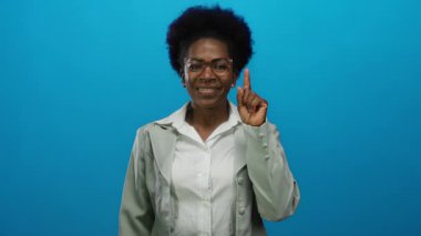 İzole edilmiş mavi arka planda, gözlük takan ve ilham anında beyaz gömlek giyen bir kadın..