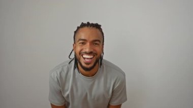 Örgülü genç adam izole edilmiş beyaz bir arka plana gülümsüyor, basit bir tişörtle mutluluk ve enerji yayıyor..