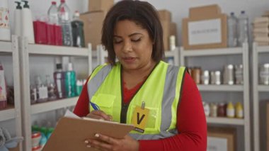 Bağış malzemeleriyle çevrili bir hayır kurumunda panoya yansıtıcı yelek giyen, gülümseyen ve gönüllü işine odaklanmış bir kadın..