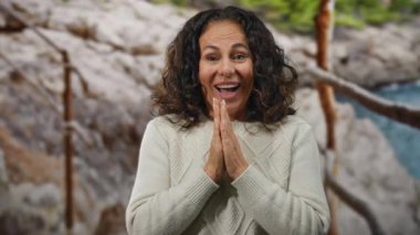 Elleriyle duaya sarılmış bir kadın, açık bir gökyüzünün altında huzurlu bir kumsalda olgun güzellik ve sükuneti sergiliyor..