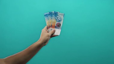 İzole edilmiş mavi arka plan duvarına karşı İsviçre frangı banknotları tutan adam, gösterişli para ve finans kavramları minimalist bir tarzda.