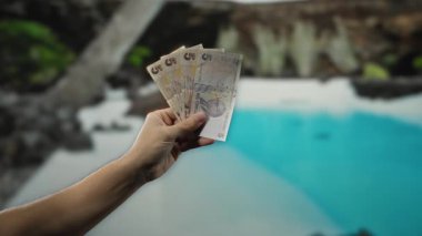 Bir tatil köyü havuzunun yanında el ele tutuşan Türk lirası banknotları lüks bir tatil sahnesi yaratıyor, açık hava ortamında canlı mavi suyla seyahat, finans ve rahatlama..