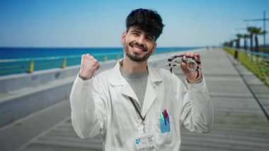 Plaj gezintisinde gülümseyen ve optometri ekipmanı tutan beyaz ceketli genç adam.
