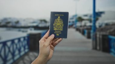 Arka planda teknelerle Kanada pasaportu taşıyan bir adam, açık havada seyahat ve kimlik sergiliyor..