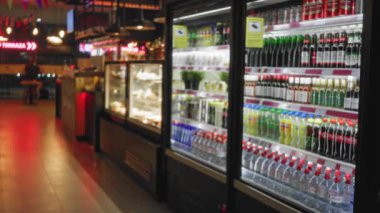 Bulanık içeceklerle dolu bir süpermarket koridoru. Arka planda canlı renkler ve soğuk içeceklerle dolu bir market atmosferini tasvir eden ışıl ışıl bokeh ışıkları..