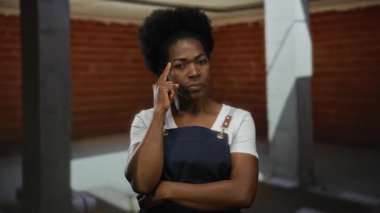 Önlüklü kadın inşaat alanına odaklanıyor. Tuğla arka plan ve düşünce ve yaratıcılık taşıyan sütunlarla evin içindeki kararlılığını gösteriyor..