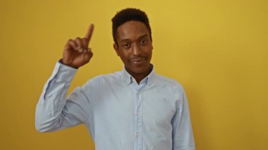 Genç Afro-Amerikan adam, gömlek giyen, ayakta duran ve gülümseyen, izole sarı arka planda, harika bir fikir ve iyi bellek ile parmak uçlarına,