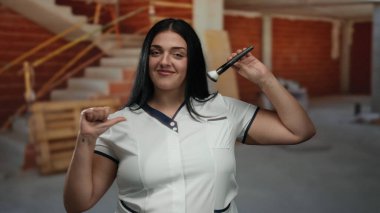 İnşaat alanında kendine güvenen bir kadın makyaj fırçasıyla gülümsüyor, eşsiz bir endüstriyel ortamda güzellik ve kendini ifade ediyor..