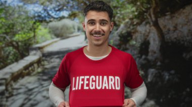 Parkta kırmızı bir cankurtaran tişörtü içinde gülümseyen genç İspanyol bir adam. Güneşli bir günde çevresi yeşillikle çevrili..