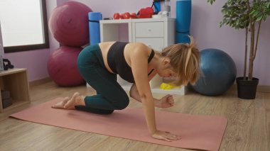 Spor salonundaki yoga minderinde egzersiz yapan bir kadın. Spor aletleriyle çevrili. Egzersiz topları da dahil..