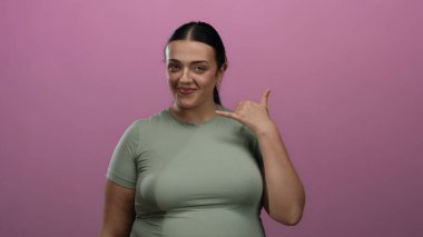 Kıvrımlı genç bir kadın, izole edilmiş pembe arka plan duvarında şakacı bir şekilde gülüyor, arkadaşlığı ve iletişimi iletiyor..