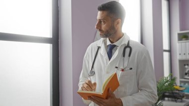 Hastane odasındaki not defterine steteskop yazan hasta bakımına ve tıbbi görevlere odaklanmış bir adam..