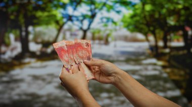 Bir şehir parkı ortamında Güney Afrika Rand banknotlarını tutan eller, açık bir şehir ortamında para ve iş kavramlarını resmediyor.