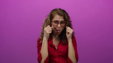 Dışlanmış pembe bir arka plan duvarından tiksinen bir kadın. Gözlüklü, yüz ifadeleriyle duygularını gösteren negatif duygular taşıyan bir kadın..