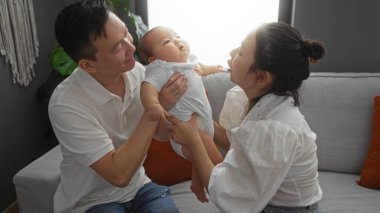 Oturma odasında, anne ve babayla birlikte bir aile, sıcak, samimi bir ortamda sevgi ve neşe ifade eden küçük bir çocuğu sıcak bir evde tutuyorlar..