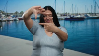 Kadın arka planda teknelerle deniz kenarında neşeli bir şekilde poz veriyor, neşeli, açık hava atmosferini somutlaştırıyor.