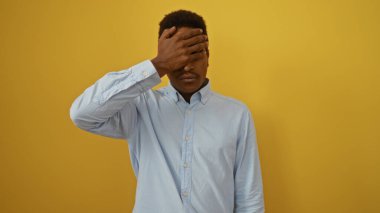 Sarı arka planda eli olan genç bir adam mavi gömlekli düşünceli ve yalnız görünüyor.