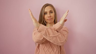 Genç bir kadın, pembe bir arka plana karşı elleri çaprazlanmış bir şekilde dur jesti yapıyor.